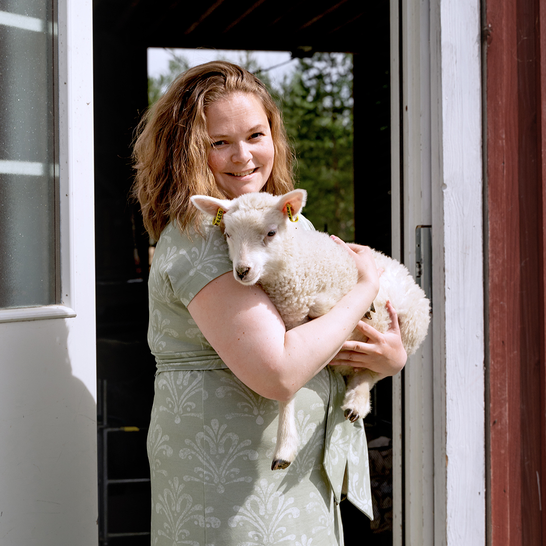 A woman holding a lamb at the front of her sheep farm in Finnish Lakeland.