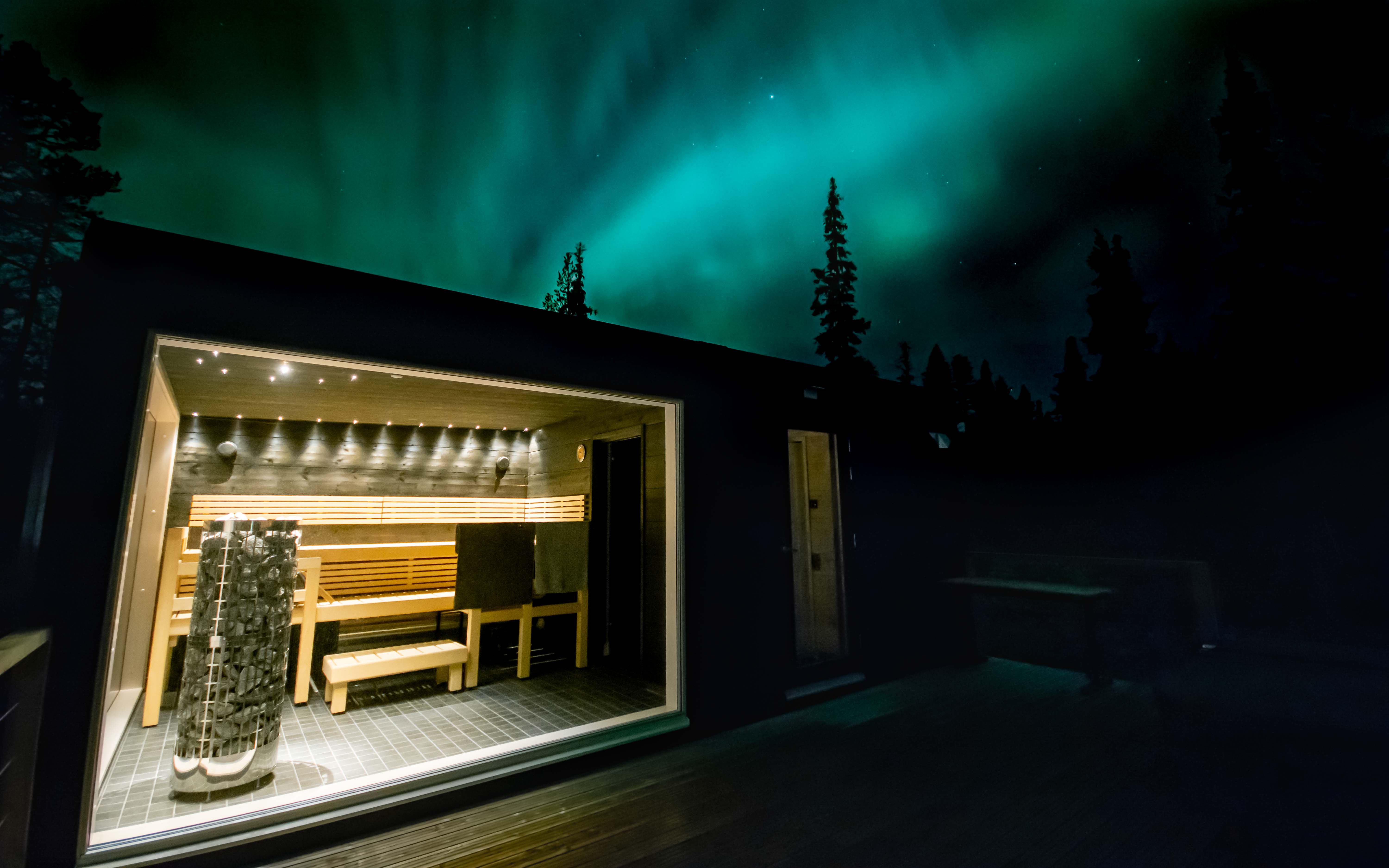 A sauna hut with a huge window under the Northern Lights.